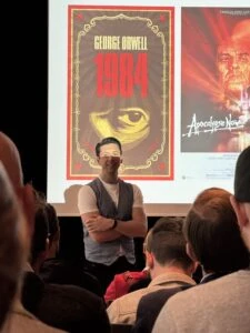 Großes Bild eines Mannes vor Filmplakaten auf einer Veranstaltung, Social Media & Podcast Marketing.