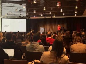 1. Präsentation bei TheAngryTeddy Kommunikationsmesse in einem dunklen Saal mit Publikum.