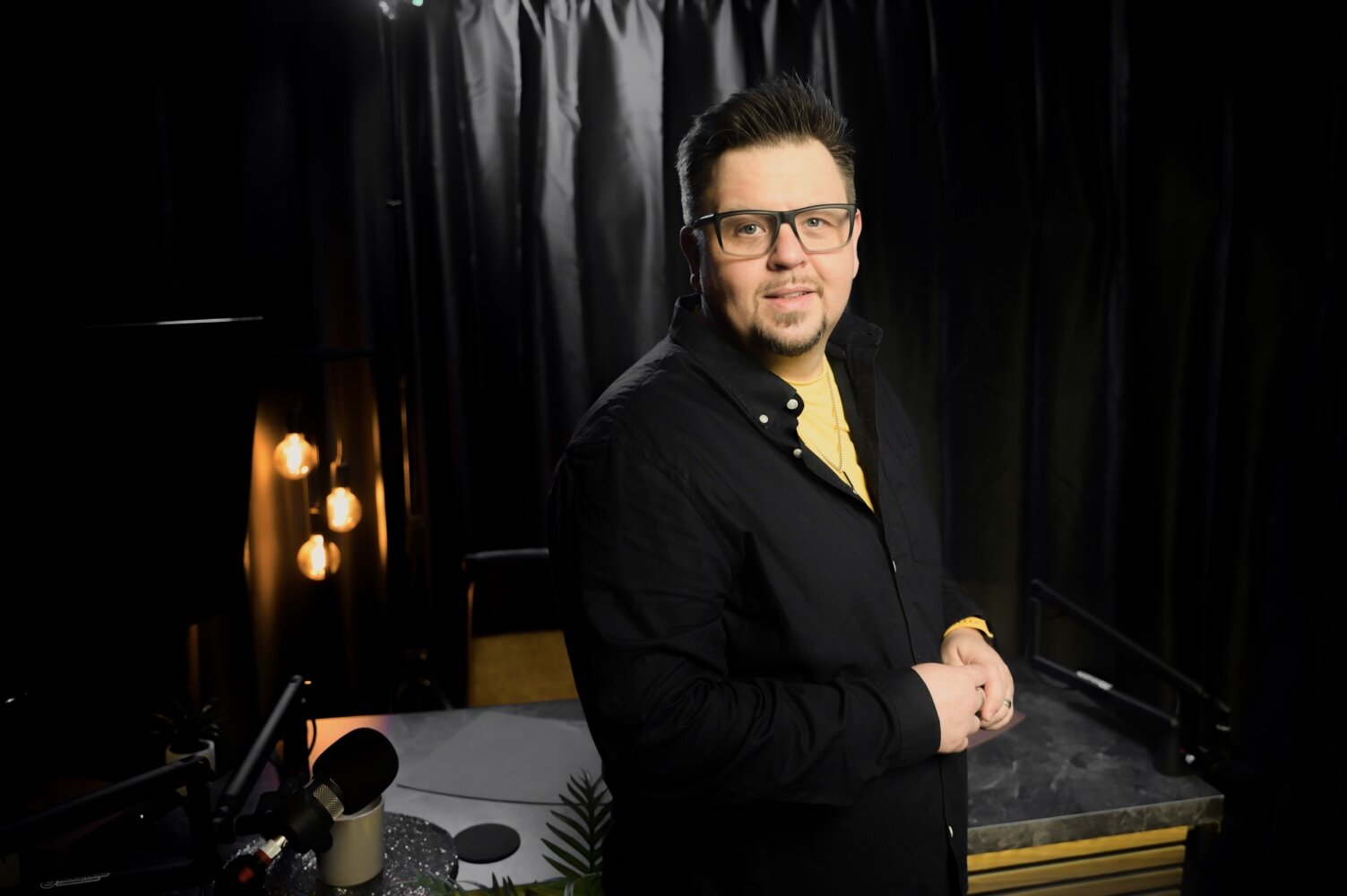 Kommunikationsprofi bei TheAngryTeddy | Social Media & Podcast Market Mann vor schwarzem Vorhang, spricht in Mikrofon bei TheAngryTeddy.