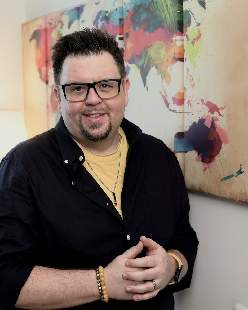 Reiseblogger mit Weltkarte im Hintergrund Reiseblogger vor bunter Weltkarte, der über globale Reisen und Kulturen spricht.